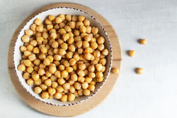 Boiled chickpeas in a beige bowl on a cutting board. Vegetarian cuisine concept. Horizontal orientation. Copy space. Top view.