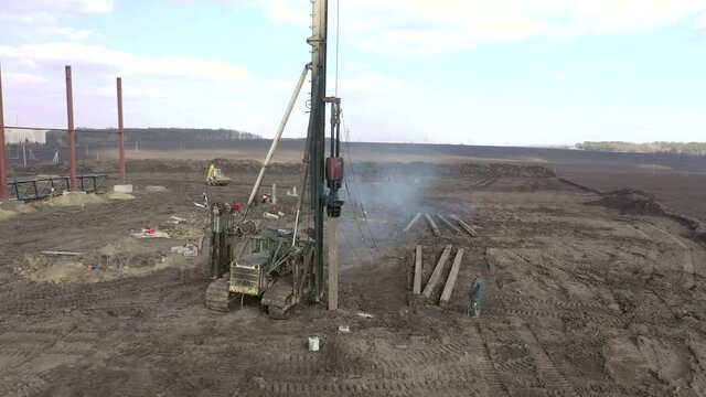 Excavation at a construction site, diesel pile driving machine with rumble and smoke drives piles deep into the ground to ensure the strength of the foundation of the future structure