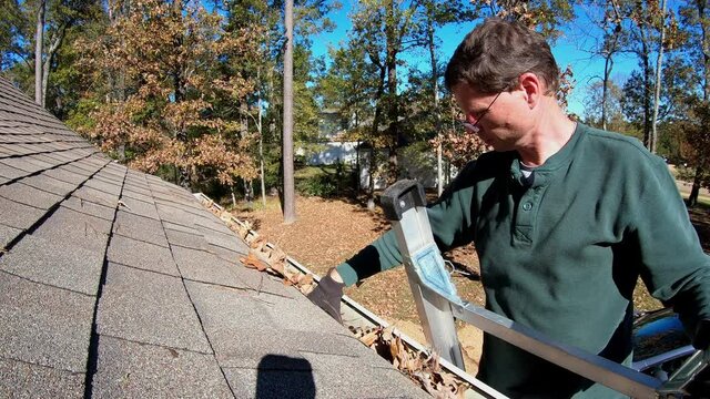 Man cleans leaves from gutter along roof.