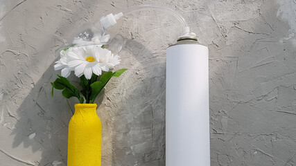 an oxygen tank stands next to a yellow vase and daisies. a breath of fresh air