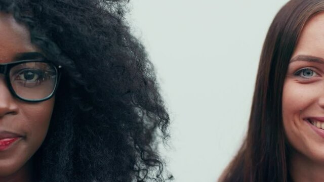 Close up portrait of beautiful african american woman with curly hair in glasses and european woman looking at camera. Half face.
