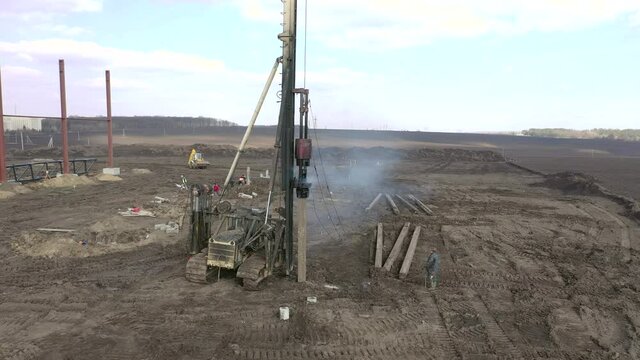 Excavation at a construction site, diesel pile driving machine with rumble and smoke drives piles deep into the ground to ensure the strength of the foundation of the future structure