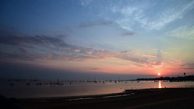 Calm sunrise over Bayshore marina in NJ with warm sunlight and vibrant colors highlighting the sailboats at mooring in the foreground.