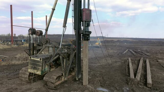 Excavation at a construction site, diesel pile driving machine with rumble and smoke drives piles deep into the ground to ensure the strength of the foundation of the future structure