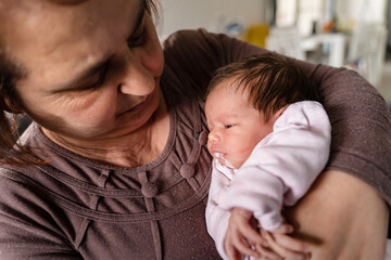 Senior caucasian woman grandmother hold newborn infant girl vomiting milk - baby overfeeding puke milk in hands of her granny at home - new life nursing and growing up concept