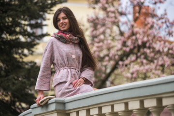 Nice girl in pastel coat and scarf on pink blossom magnolia tree background