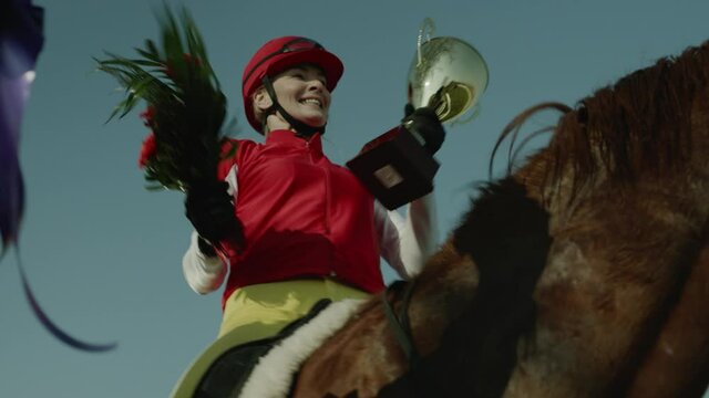 Jockey Woman Celebrate Victory in Race Tournament. Sportswoman Sitting on Horse Horseback, Kissing and Showing Award to Fans. Girl Stallion Rider Happy and Positive Emotion Tracking Shot Slow Motion