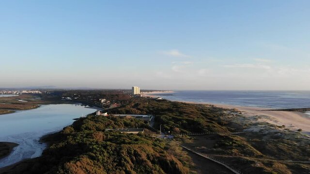 DRONE AERIAL FOOTAGE: The Northern Litoral Natural Park in Ofir, Esposende, Portugal. Wooden boardwalk and the Ofir Towers in the background. Sea, beach boulders, pebble shore and waves at sunset.