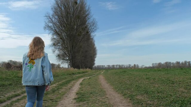[4k] lifestyle portrait of cute blone woman in denim with flower on her back walking in green nature