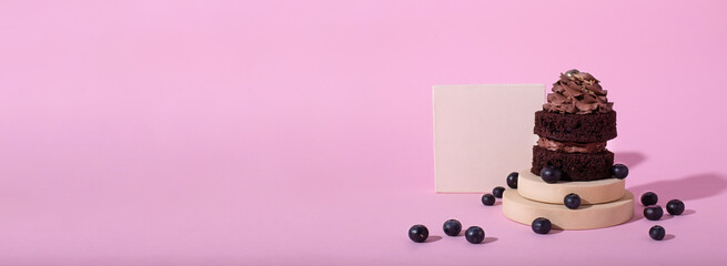 Horizontal banner with gluten free cake with blueberry and carob. Homemade chocolate cake with raw berries on modern circle and square podiums on pink background. Creative food photo. Copy space