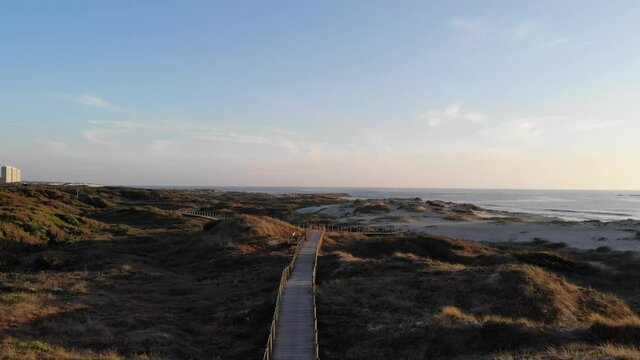 DRONE AERIAL FOOTAGE: The Northern Litoral Natural Park in Ofir, Esposende, Portugal. Wooden boardwalk and the Ofir Towers in the background. Sea, beach boulders, pebble shore and waves at sunset.