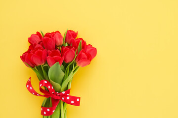 Red tulips bouquet decorated with ribbon on a yellow background. Mothers Day, Valentines Day concept