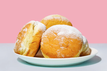 Classic European donuts. Plate with powdered doughnuts on pink background. Sweet traditional german, polish pastries.