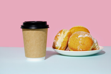 Donuts sprinkled with powdered sugar and paper coffee container on trendy minimal coloured background. Takeaway food and fastfood concept.