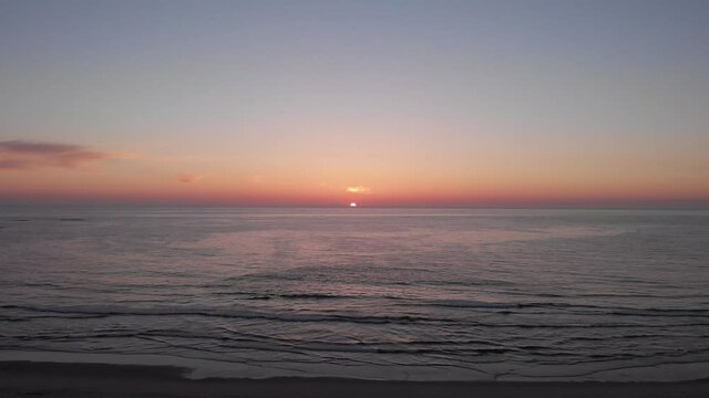 DRONE AERIAL FOOTAGE: Sea, beach boulders and waves at sunset. Beautiful sunset with flying birds. Waves crashing on sandy beach. Beach with sand dunes and dusk sky in Ofir, Fao, Portugal. 