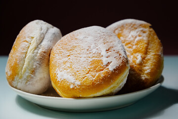 Classic donuts sprinkled with powdered sugar. Plate with powdered doughnuts on dark background. Sweet traditional german, polish pastries. 