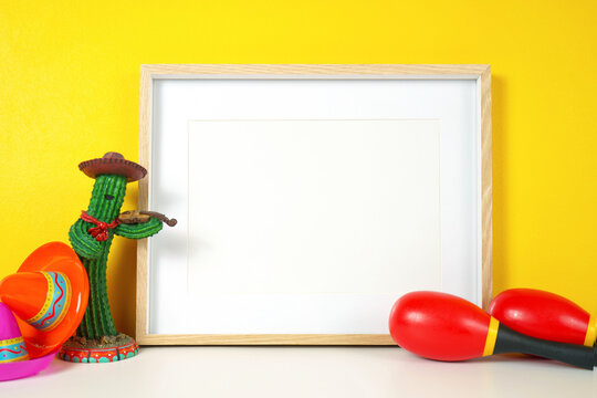 Cinco de Mayo horizontal frame against a festive yellow background, styled with colorful maracas and sombrero hats. White product mock up with negative copy space for your text or design here.