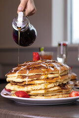 pouring syrup on a stack of pancakes for brunch 