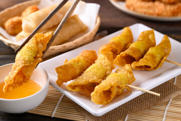Asian deep fried crispy wonton stuffed with minced pork, quail egg and shrimp dipping with chili sauce by chopsticks