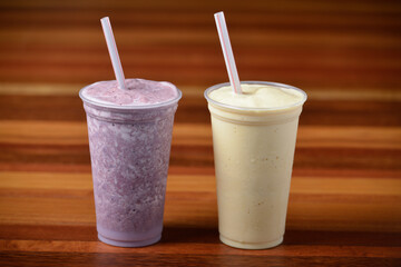 Fruit smoothies in glasses and plastic straws on a dark wooden table.