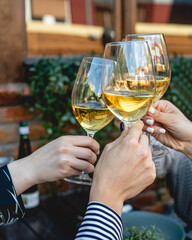 close up on hands of unknown group of caucasian women holding glasses of white wine toasting while sitting at restaurant in day outdoor female friends celebrating