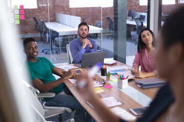Diverse group of creative colleagues in meeting room listening presentation taking notes