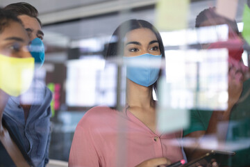 Diverse group of creative colleagues wearing face masks brainstorming in meeting room