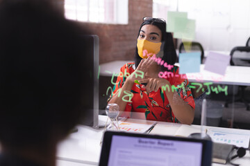 Mixed rase businesswoman wearing mask pointing at glass wall