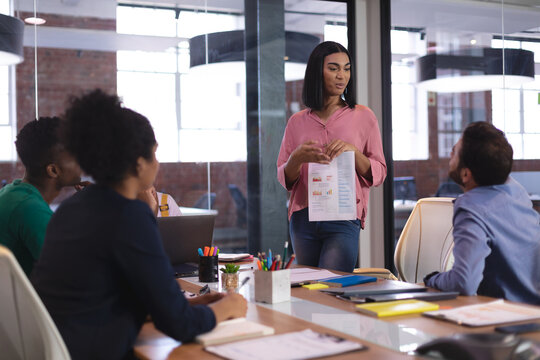 Mixed race woman giving presentation to diverse group of colleagues in meeting room