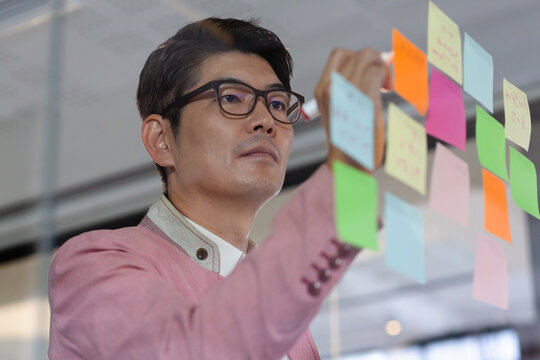 Stylish asian businessman writing notes on glass wall