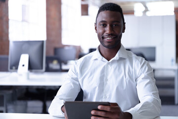 Portrait of happy casual african american businessman using tablet and smiling to camera