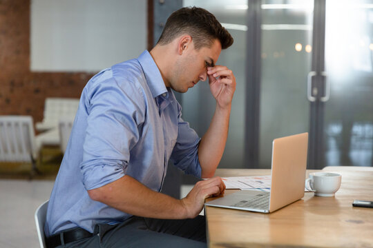 Casual caucasian businessman sitting at desk, thinking and using laptop