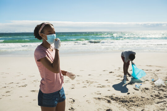 African american race couple wearing face masks collecting rubbish from the beach - Powered by Adobe