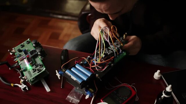 DIY, the machine on electronic control. Home experiments, robotics, smart engineer. Toy for the child. A man collects repairs to an electronic device. Wires, motherboard, batteries closeup