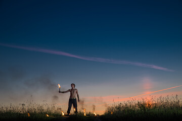 Man stands with signal torches against dark sunset sky