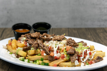 Large plate of Asada french fries covered in cheese served with dipping sauce will tempt everyone.