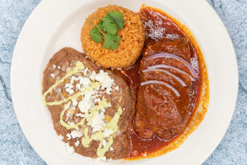 Overhead view of large slap of Chile Colorado entree meat, refried beans, and rice drenched in the red sauce.
