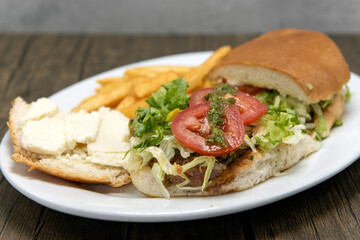 Large Churrasquito sandwich lies open with juicy tomato slices on top served with french fries.