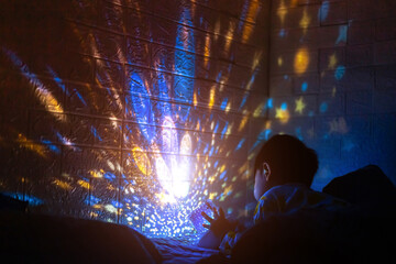 Little boyl in his room with night light projecting stars on room ceiling. Children read before bedtime.