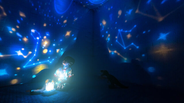 Little boyl in his room with night light projecting stars on room ceiling. Children read before bedtime.