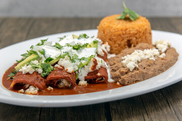 Chicken enchiladas smothered in red sauce served with refried beans and rice for a tasty Mexican food meal.