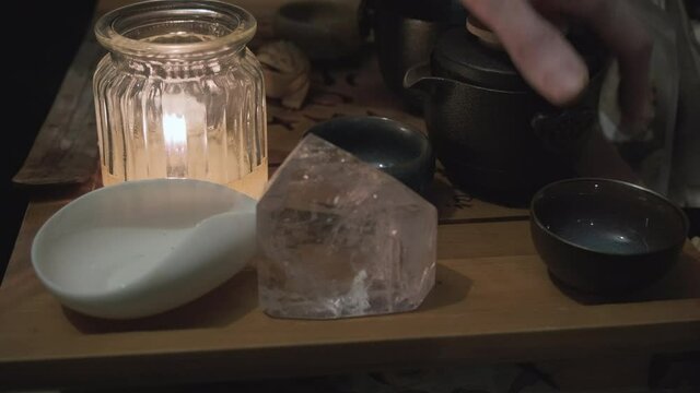 On the tea board there is a stand a magic crystal and a candle. Man hand pours a drink into clay cups. Close up shot. The concept of Chinese and Japanese tea ceremonies, divination and magical ritual