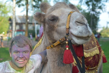 On the street, a teenager stands next to a camel.