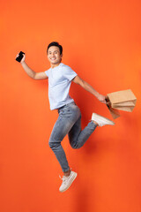 Asian man holding smartphone and shopping bag while jumping