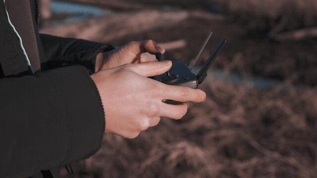 A person using a controller with a smart phone mounted to it to operate a drone UAV DJI Mini quad copter with no logo or symbols on equipment slow motion