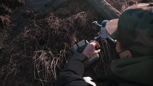 Over the shoulder view of a person powering on his small dji mini drone UAV quadcopter aircraft with grass sand mud logs in in the background