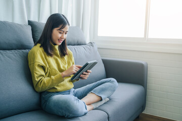 Beautiful Asian happy smile woman using tablet technology playing entertainment internet browsing social media website studying business, in free time domestic home lifestyle comfy in living room