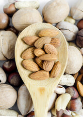 Nuts almonds in a wooden spoon on the background of a scattering of different nuts assorted nuts vertical