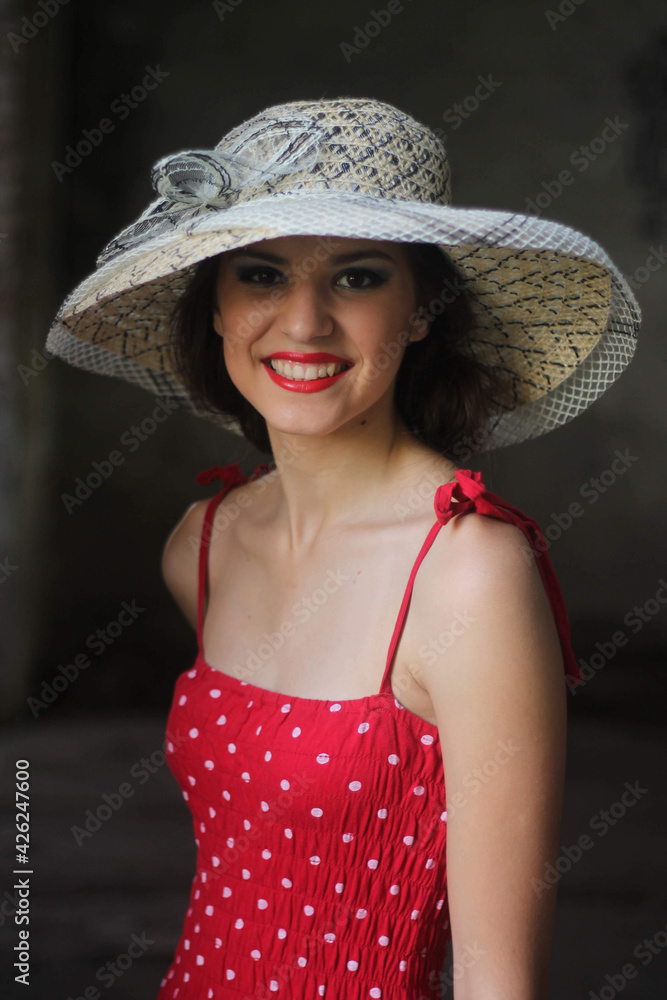 Sticker Vertical shot of a beautiful young Caucasian lady wearing a red polka-dot dress and a summer hat