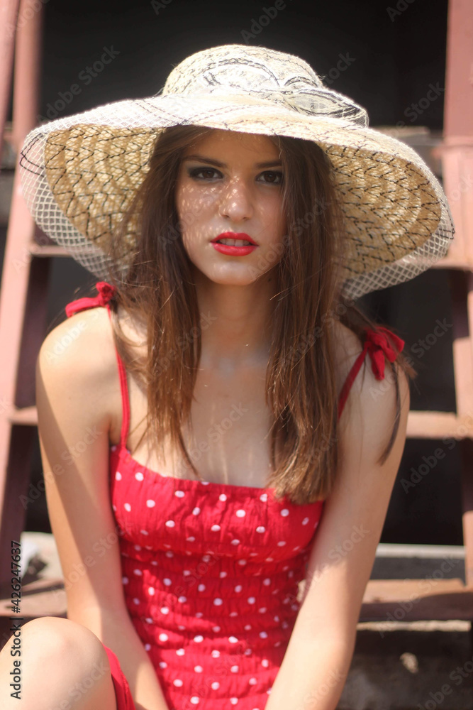 Canvas Prints Vertical shot of a beautiful young Caucasian lady wearing a red polka-dot dress and a summer hat